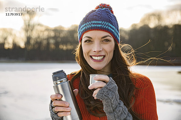 Porträt einer lächelnden Frau  die im Winter ein Heißgetränk aus der Thermoskanne trinkt.