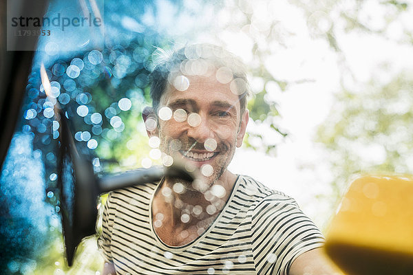Porträt eines lächelnden  reifen Mannes  der die Windschutzscheibe seines Autos wäscht.