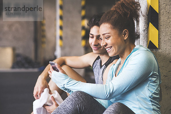 Zwei lächelnde Athleten teilen sich ihr Handy im Fitnessstudio.