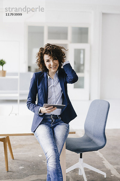 Geschäftsfrau im Büro auf dem Schreibtisch sitzend  mit digitalem Tablett
