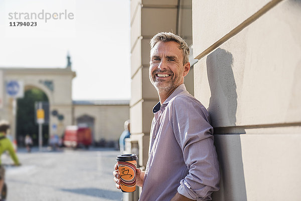 Lächelnder Mann mit Kaffee zum Mitnehmen in der Stadt