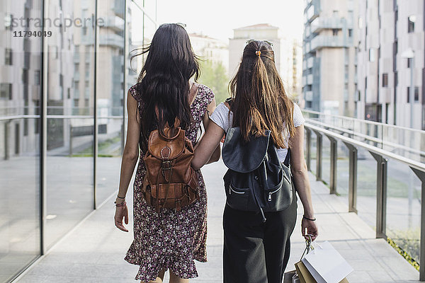 Zwei junge Frauen mit Rucksäcken und Einkaufstaschen laufen durch die Stadt.