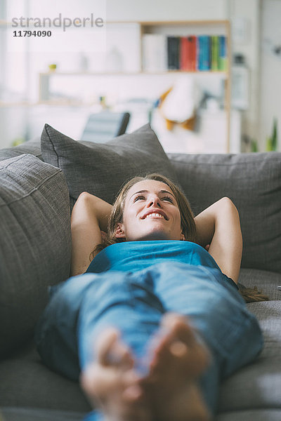 Lächelnde junge Frau auf der Couch zu Hause liegend