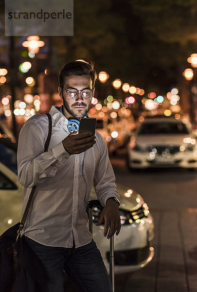 Junger Mann in der Stadt  der nachts sein Handy überprüft.