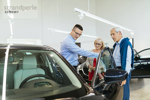 Seniorenpaar im Gespräch mit Verkäufer im Autohaus