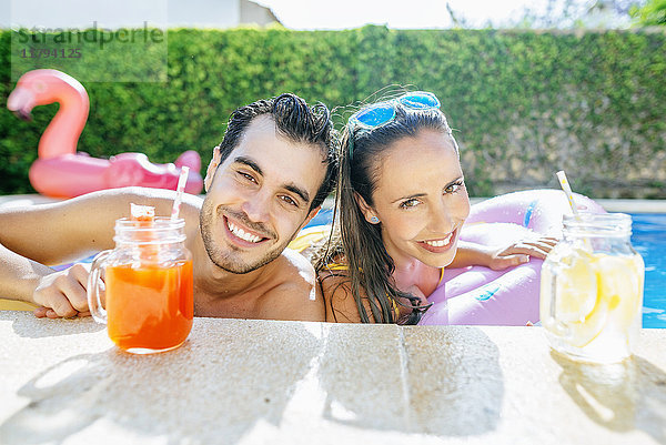 Glückliches Paar im Schwimmbad mit Getränken am Pool