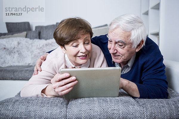 Seniorenpaar auf der Couch liegend mit digitalem Tablett