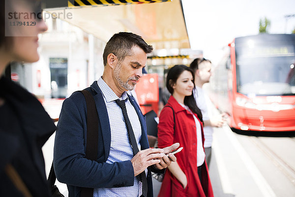 Geschäftsmann mit Smartphone wartet an der Bushaltestelle