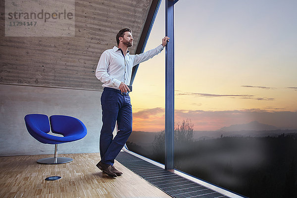 Geschäftsmann im Dachgeschoss mit Blick aus dem Fenster bei Sonnenuntergang