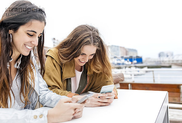 Zwei glückliche junge Frauen  die mit ihren Smartphones Nachrichten senden