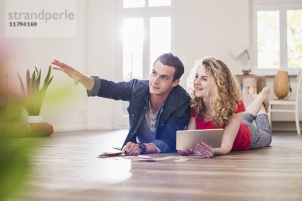 Junges Paar in neuem Zuhause auf dem Boden liegend mit Tablette aus Farbmusterauswahl