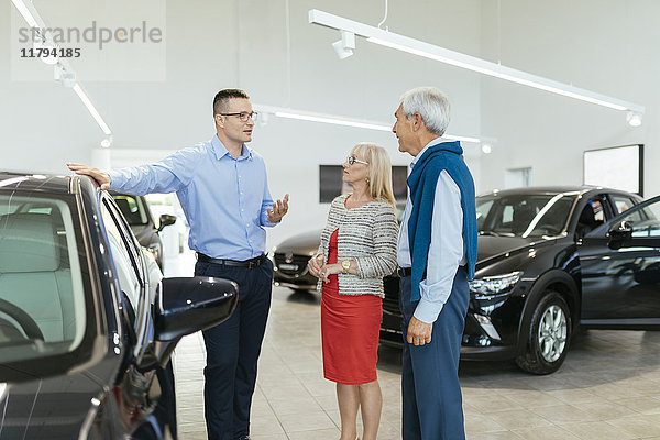 Seniorenpaar im Gespräch mit Verkäufer im Autohaus