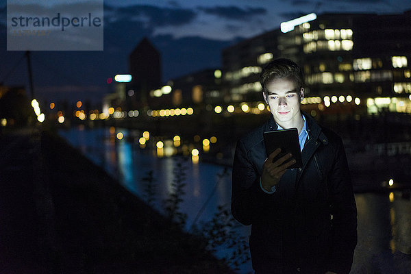 Junger Mann mit Tablette im Freien bei Nacht
