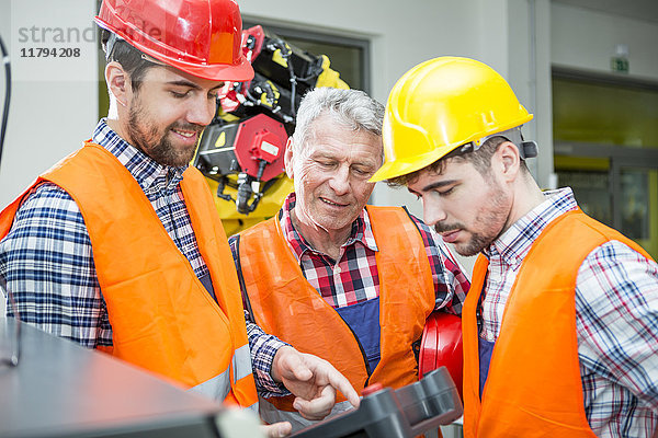 Drei Männer in der Fabrik im Gespräch mit Industrieroboter im Hintergrund