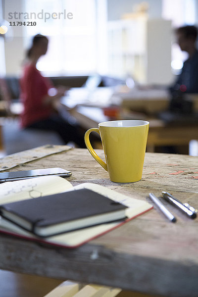 Notebook und Kaffeetasse im modernen informellen Büro mit Mann und Frau im Hintergrund