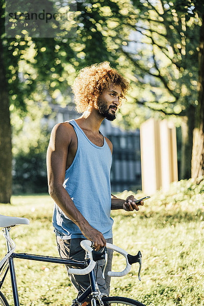 Junger Mann mit Fahrrad und Handy im Park