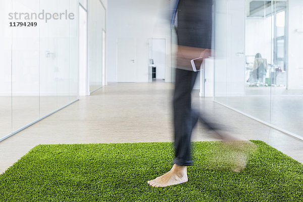 Ein reifer Geschäftsmann  der barfuß auf einem Grasteppich im Büro läuft.