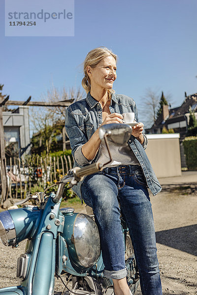 Lächelnde Frau mit Oldtimer-Motorrad bei einer Kaffeepause