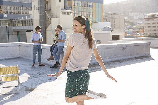 Tanzende Frau auf der Dachterrasse mit Freunden im Hintergrund