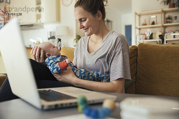 Mutter hält ihr neugeborenes Baby zu Hause neben dem Laptop
