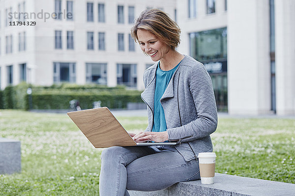 Glückliche Frau im Freien mit Laptop und Kaffee zum Mitnehmen