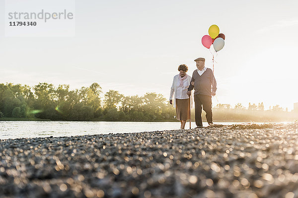 Seniorenpaar mit Ballons  die am Flussufer spazieren gehen