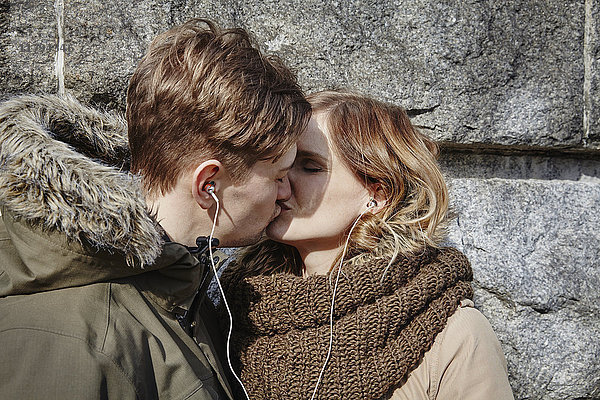 Junges Paar  das sich die Ohrstöpsel an der Steinmauer küsst