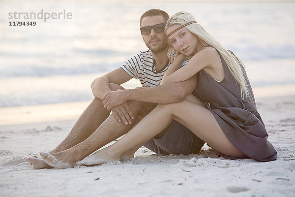 Junges Paar am Strand sitzend  umarmend