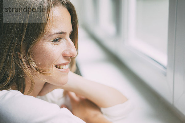 Lächelnde junge Frau schaut aus dem Fenster