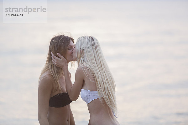 Zwei junge Frauen  die sich am Meer küssen.