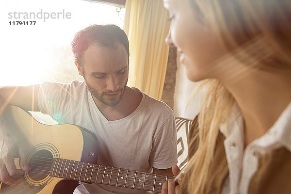 Mann  der zu Hause Gitarre spielt  während seine Freundin ihn beobachtet.