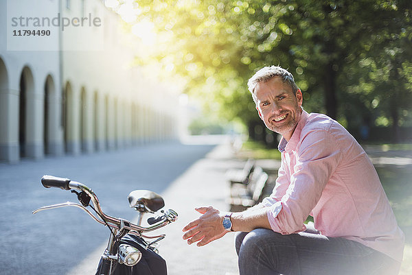 Porträt eines lächelnden Mannes mit Fahrrad auf der Parkbank