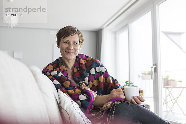 Porträt einer lächelnden Frau bei einer Tasse Kaffee auf der Couch