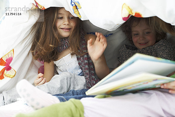 Drei kleine Kinder mit Buch zusammen unter der Decke