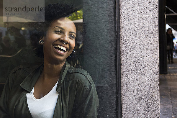 Porträt einer lachenden jungen Frau  die durch das Fenster eines Cafés schaut.