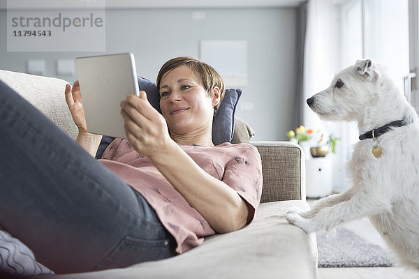 Porträt einer lächelnden Frau  die auf der Couch liegt und dabei den Hund beobachtet.