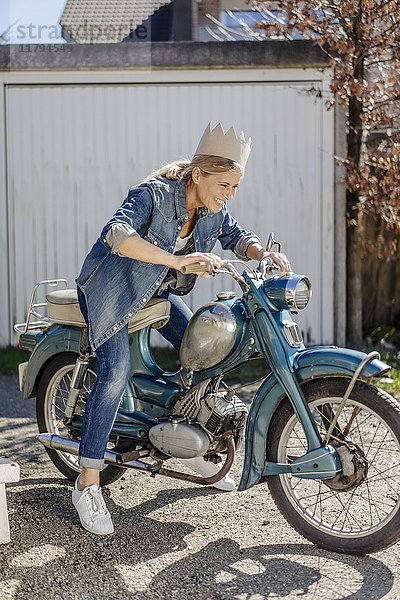 Glückliche Frau auf Oldtimer-Motorrad mit Krone