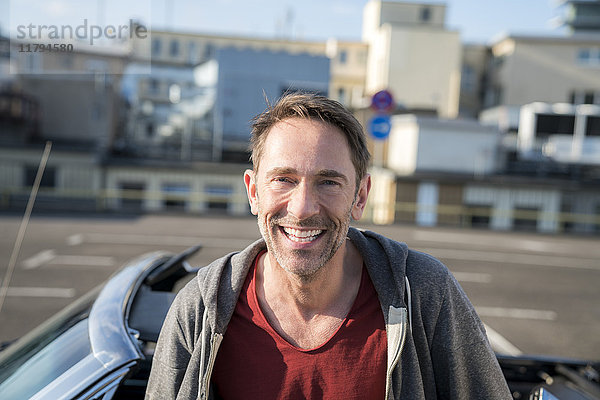 Porträt des lachenden reifen Mannes mit Stoppel vor seinem Sportwagen
