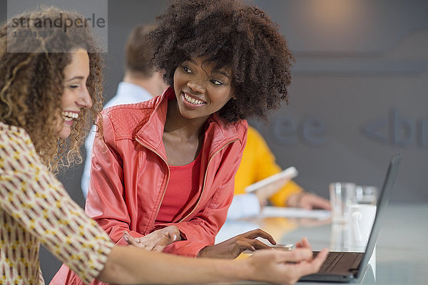Zwei glückliche Frauen im Büro teilen sich einen Laptop