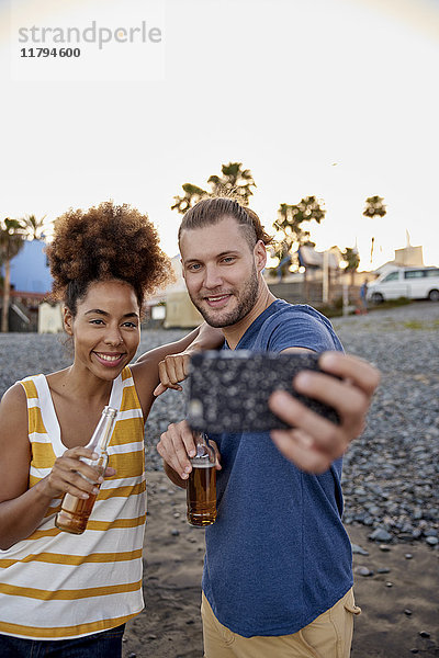 Zwei Freunde mit Bierflaschen  die Selfie am Strand mitnehmen.