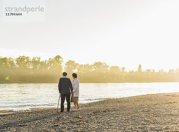 Seniorenpaar steht am Flussufer bei Sonnenuntergang