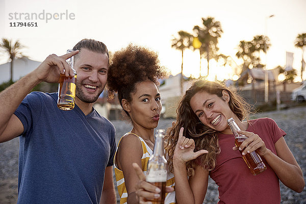 Drei Freunde mit Bierflaschen am Strand bei Sonnenuntergang