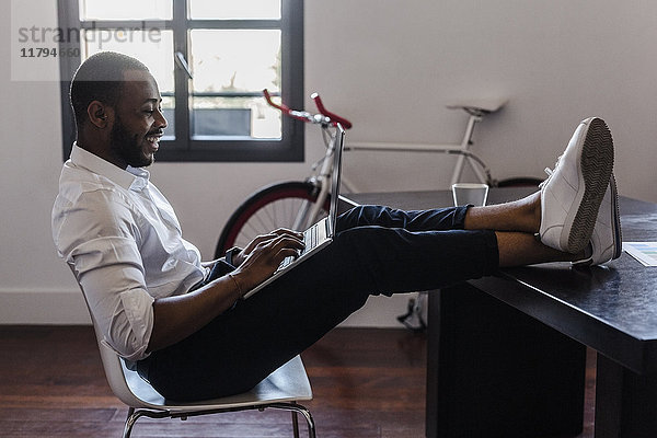 Mann mit Laptop im Home-Office mit Füßen auf dem Schreibtisch