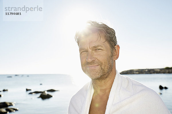 Porträt eines lächelnden Mannes mit Handtuch vor dem Meer