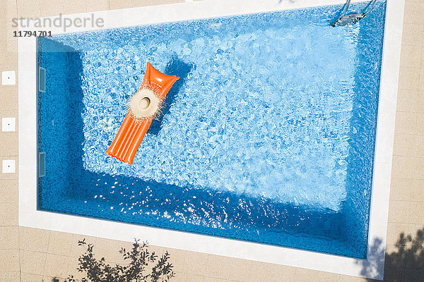 Strohhut auf orangefarbenem Luftbett im Schwimmbad  Draufsicht