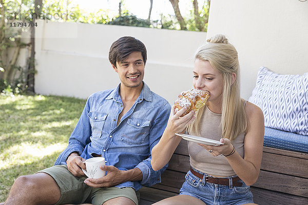 Lächelnder Mann sitzt auf der Terrasse und beobachtet die Freundin beim Essen.