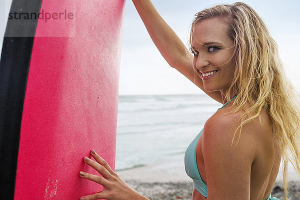 Lächelnde Frau am Strand mit Surfbrett