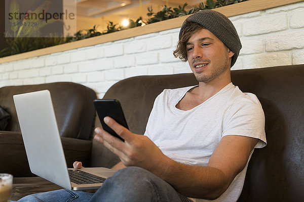 Junger Mann mit Handy und Laptop in einem Cafe