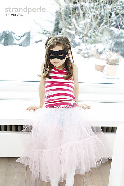 Porträt eines kleinen Mädchens mit Maske auf dem Fensterbrett sitzend
