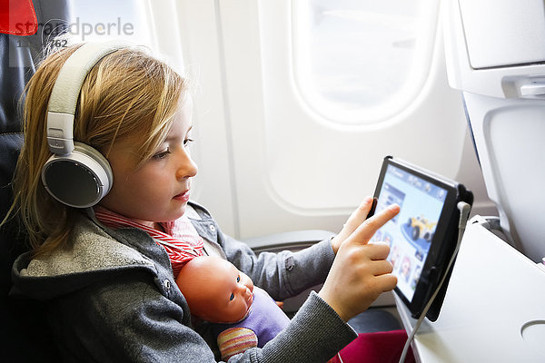 Kleines Mädchen  das im Flugzeug sitzt und etwas auf einem digitalen Tablett sieht.